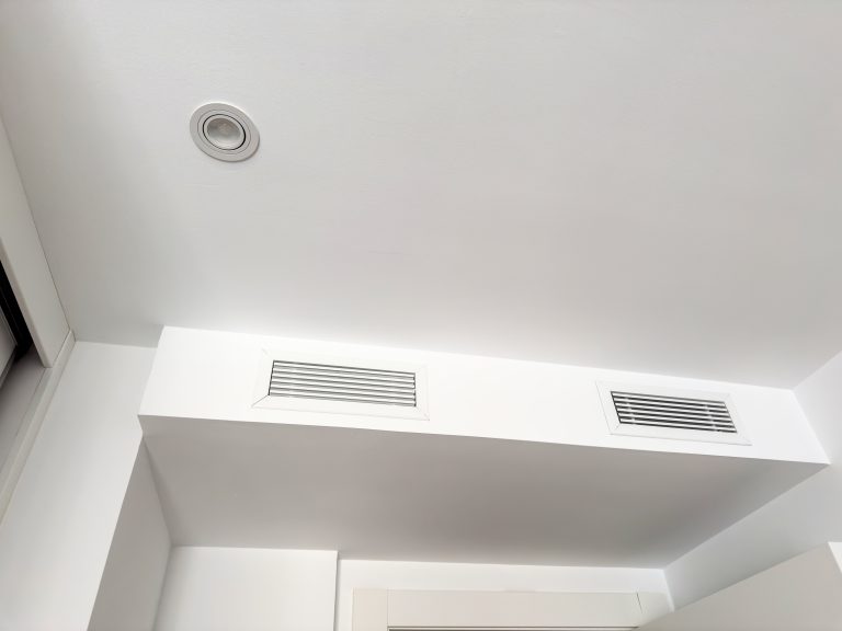 A white ceiling bulkhead with two linear air diffusers and a recessed downlight. Concealed HVAC ventilation and lighting.